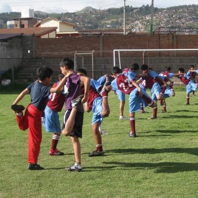Un voluntario dirigiendo a niños durante un calentamiento en nuestro voluntariado de deportes en Perú. Voluntario deportivo en Perú dirigiendo una sesión de calentamiento.